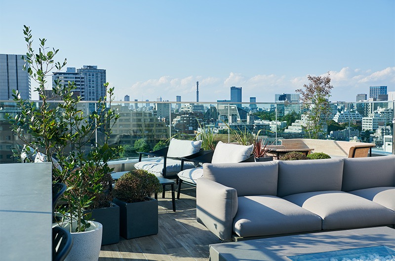 都心の景色を一望できる、緑とソファが配置された屋上テラス