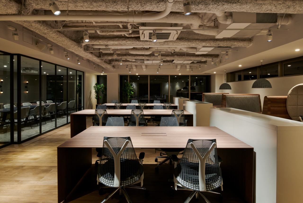 配管むき出しの天井と木製デスクがおしゃれなオフィス内観