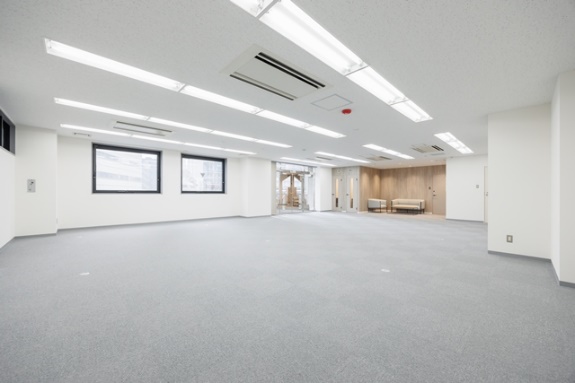 白い壁と明るい照明が特徴の、がらんとした改装前のオフィス。