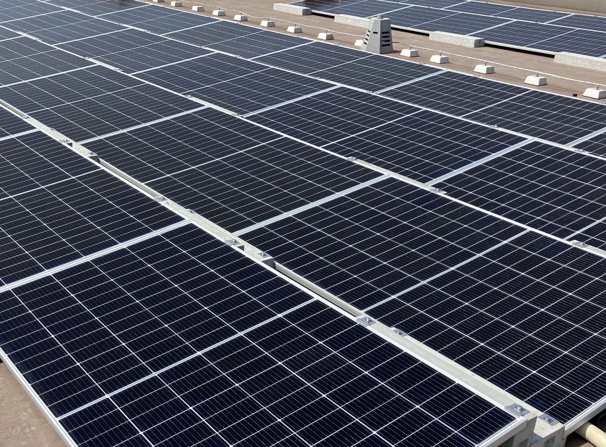 A large-scale solar panel installation on the rooftop of a building in a street with factories and buildings.