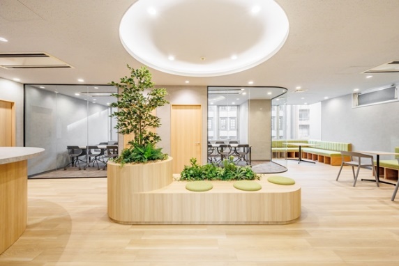 A modern office lounge with a bench in the center featuring plants.